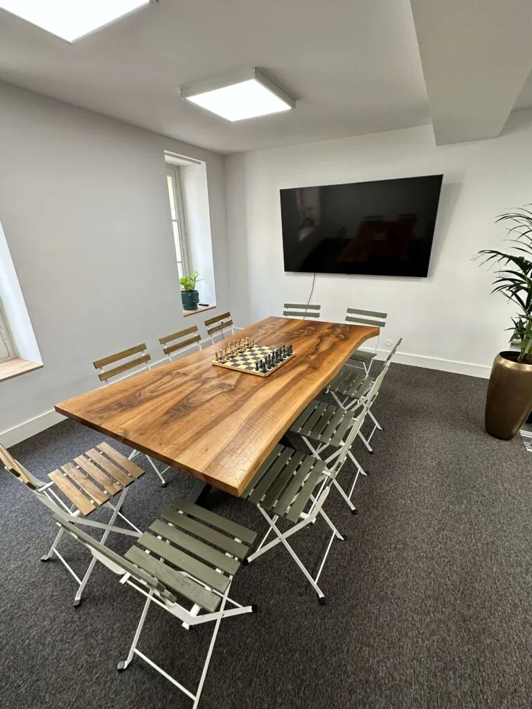 Salle avec grande table en bois, chaises pliantes et écran mural